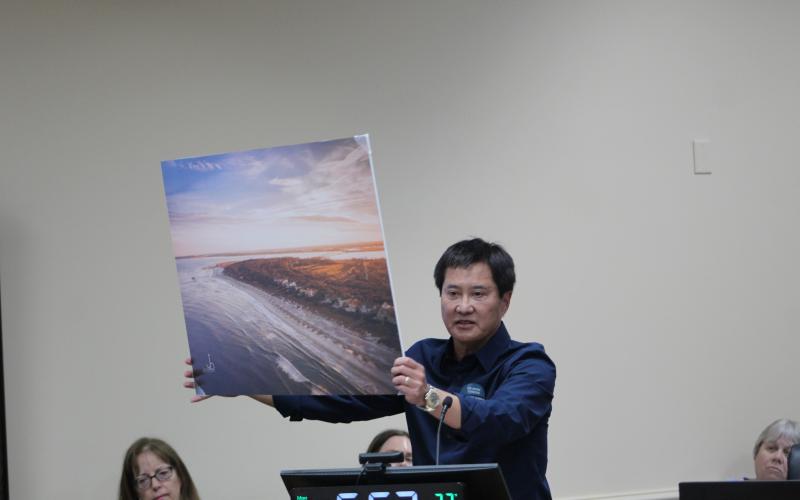 Peter Brual showed the BOCC and the audience a picture of the south end of Amelia Island, imploring commissioners to vote against a settlement that would allow 85-foot condominiums to be built. “This is a picture of the crown jewel of the whole area,” Brual said. “It’s why we’re here. Think about, if Riverstone wins, what this might look like. Can you see it? Towers over canopy treetops. Please vote no settlement.”  Photo by Julia Roberts/News-Leader