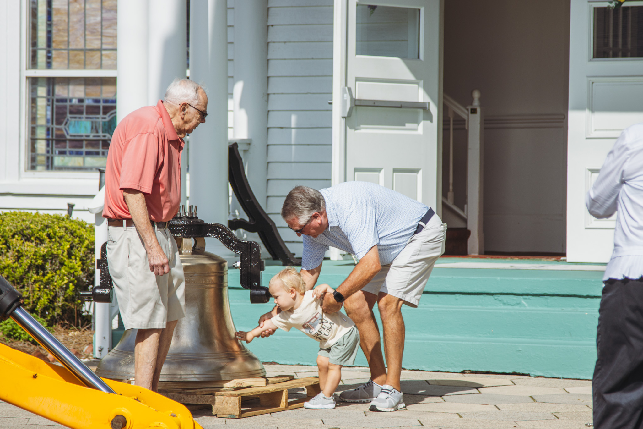 Betz Williams touches the restored church bell Tuesday. Williams and his family, including his grandpa Ken Byrns, right, and great grandfather Tom Spayde, left, are members of First Presbyterian Church. William's family said he was baptized around six months ago. Photo by Ashley Chandler/News-Leader
