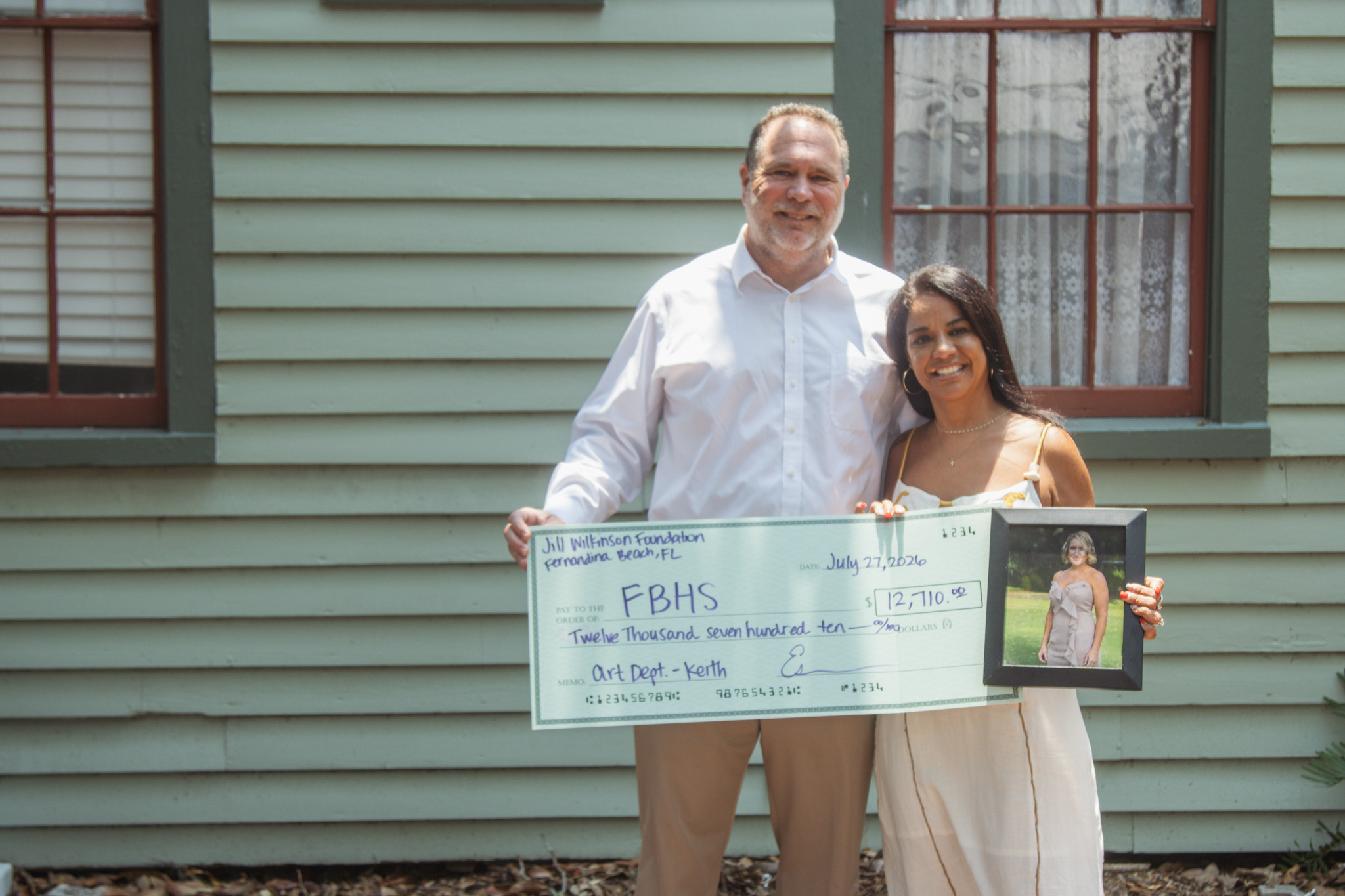 The fourth annual Fernandina Beach Art Department fundraiser and silent auction raised nearly $13,000 for the school program. From left, Todd and Esmerelda McDonald pose with and a photo of their friend Jill Wilkinson and the ceremonial check presented to the Fernandina Beach Art Department. Photo by Ashley Chandler/News-Leader