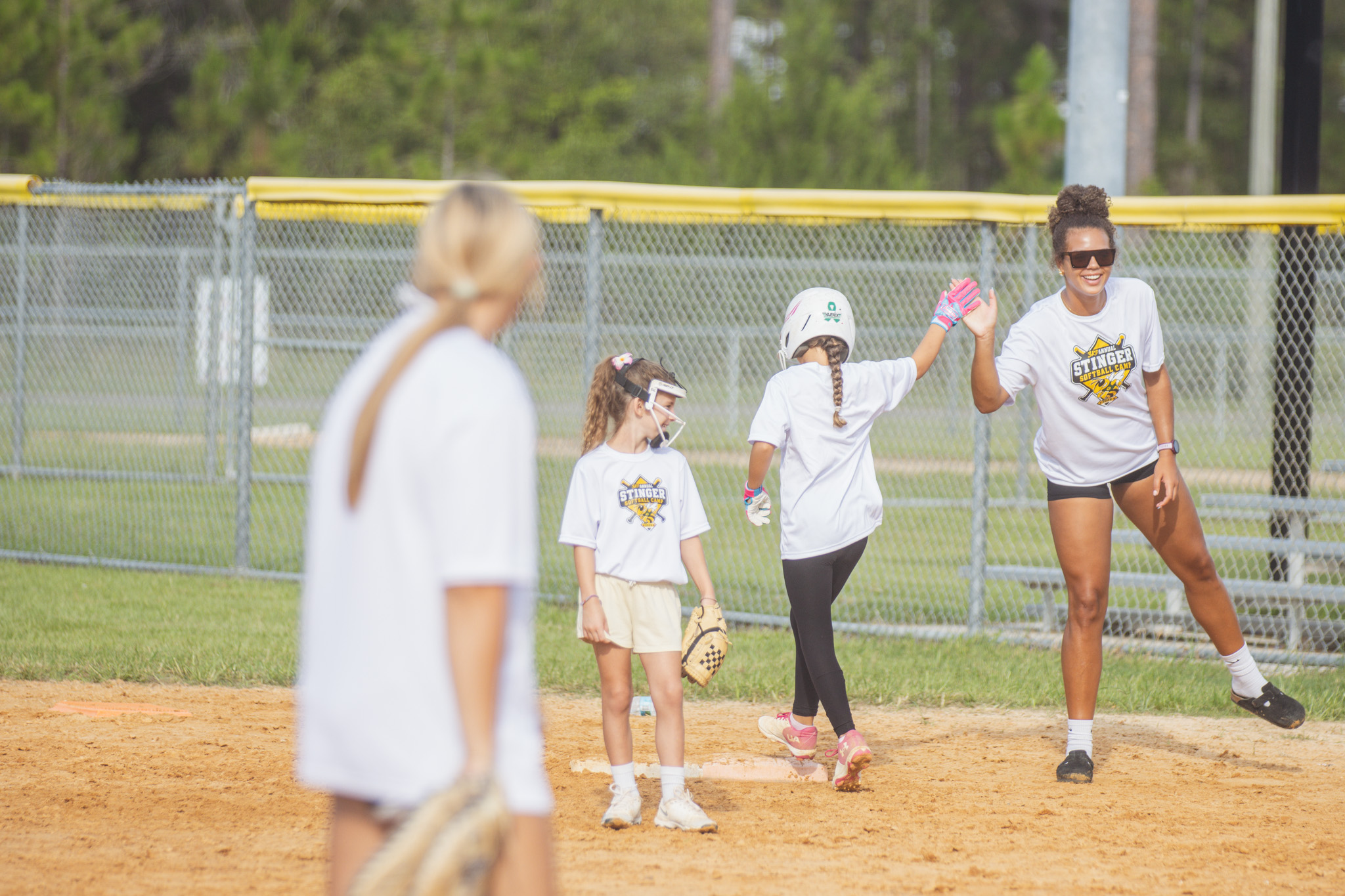 YHS’s Carmen Overstreet, right, high fives a camp participant as she makes it to first base Thursday. Photo by Ashley Chandler/News-Leader