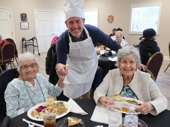 NCCOA Board Chair Ken Saitow serves up Thanksgiving cheer to Miss Suzanne (left) and Miss Marlene.