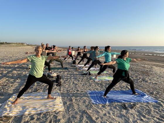 Beach yoga participants in warrior 2 pose.