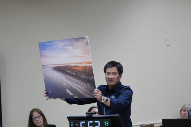Peter Brual showed the BOCC and the audience a picture of the south end of Amelia Island, imploring commissioners to vote against a settlement that would allow 85-foot condominiums to be built. “This is a picture of the crown jewel of the whole area,” Brual said. “It’s why we’re here. Think about, if Riverstone wins, what this might look like. Can you see it? Towers over canopy treetops. Please vote no settlement.”  Photo by Julia Roberts/News-Leader