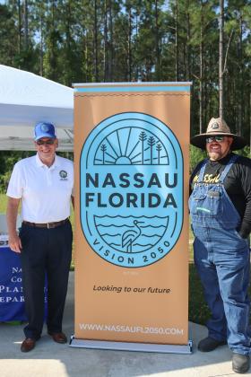 Nassau County commissioners John Martin and Clint Farmer pose next to the Vision 2050 flag at the Vision 2050 popup tent during the YMCA Healthy Kids Day event on April 20.  Photo by Ashley Chandler/News-Leader