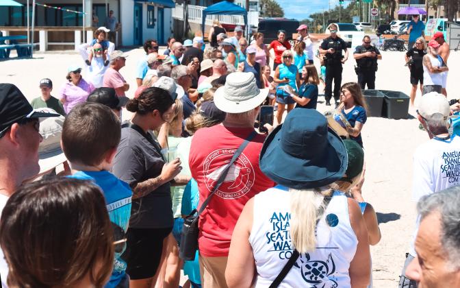 Attendants of the sea turtle release Thursday watch Sydney Milburn, rehabilitation technician I, carry Gamby, left, and Dr. Briana-Lee Shaffner, associate veterinarian, carry Quintet, two rehabilitated sea turtles. The two were released in the ocean on Main Beach back to the Atlantic. Ashley Chandler/News-Leader