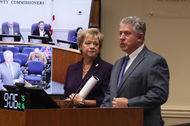 Doug Adkins, right, talks Oct. 16 at the Nassau County Board of County Commissioners meeting after the board proclaimed October 2024 as Emily Adkins Blood Clot Awareness Month. Janet Adkins, Supervisor of Elections, right, listens. Photo by Ashley Chandler/News-Leader
