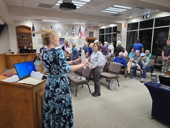 Kelly Yates shows photos of what she says are events targeting children by the LBGTQ community. In response to what they believe is hate speech, people attending the meeting stood with their backs to the speaker. Photo by Julia Roberts/News-Leader