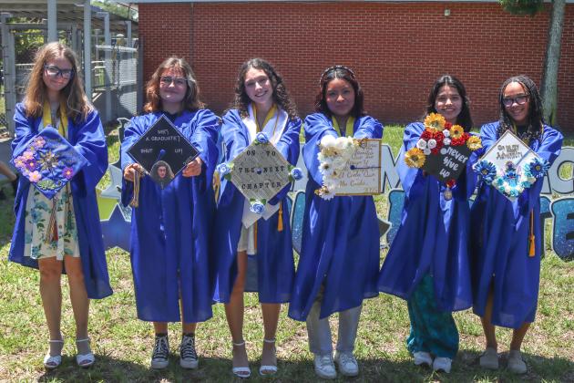 A few Fernandina Beach High School seniors hold up their decorated caps Thursday at Southside Elementary. Photo by Ashley Chandler/News-Leader