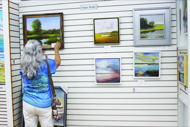 Artist Ginger Bender hangs art on her wall at the gallery.