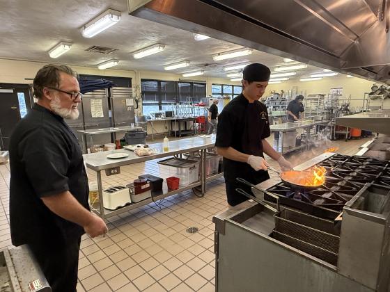 Chef Michael Gass instructs a student, who cooks a chicken breast.
