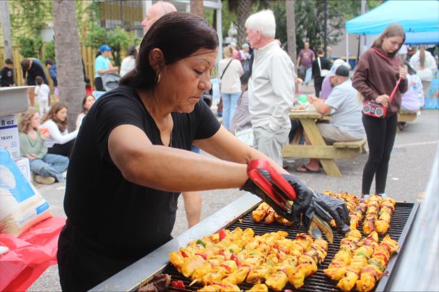 A festival vendor cooks and serves Mexican chicken skewers. 