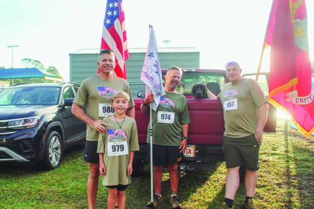 Steven Stanevich, Ivan Stanevich, Webb Skelton, Nolan Maccabee, and dog "socks" prepare for the 5K with a large American Flag and U.S Marine Corps flag.