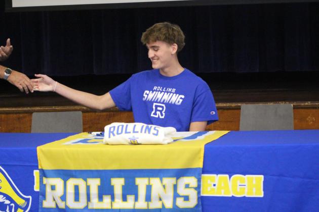 Logan Cook shakes hands with the FBHS swim coach while signing his commitment letter to swim at Rollins University. By Marisa DeMar/News-Leader
