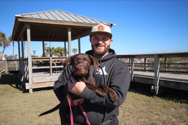 Andrew Ensign of Sentinel K9 Academy holds Daisy, the 4-month-old Labrador retriever he is training to be an autism assistance dog, at Main Beach on Dec 31. Photos by Marisa DeMar