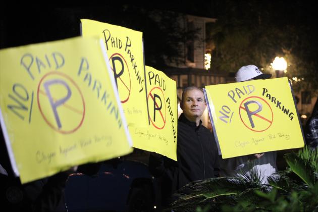Citizens hold “No-paid parking” signs outside of City Hall as the ordinance is read at the meeting on Tuesday night. By Marisa DeMar/News-Leader