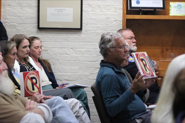 Meeting attendees hold anti-paid parking signs in their seats at Tuesday's meeting. By Marisa DeMar/News-Leader