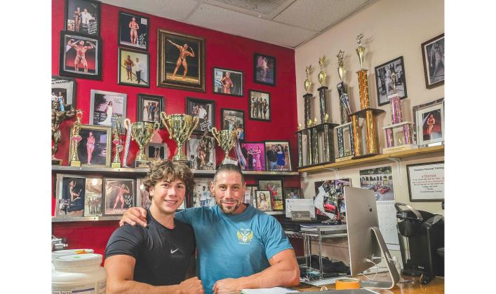 From left, Joseph Voss-Danker and his father Fred Danker pose behind the desk in their personal training facility in Fernandina Beach. Photo by Ashley Chandler/News-Leader