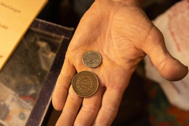 Nick Drakus, co-owner of Ice House Antiques, shows the size difference between a MacGregor Medallion and a U.S. quarter. Photo by Ashley Chandler/News-Leader