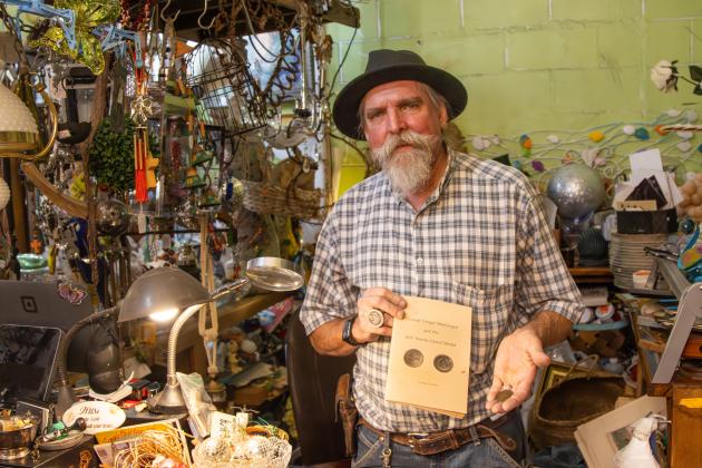 Nick Drakus, co-owner of Ice House Antiques, holds a MacGregor Medallion and the book he came across that tells the history of the medals. Photo by Ashley Chandler/News-Leader