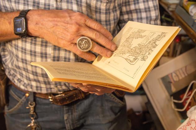 Nick Drakus, co-owner of Ice House Antiques, scans through the book he came across that tells the history of the medals. Photo by Ashley Chandler/News-Leader