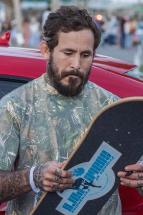 Ecuadorian mixed martial artist, Marlon “Chito” Vera signs a skateboard for Mike Nichols, Treasurer of Friends of Fernandina Skatepark at Main Beach Park during the Gumball 3000