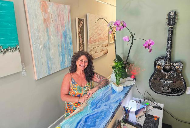 Julie Delfs stands beside the custom-made front desk at Art Amelia, her artwork hangs on the wall to each side of her. Photo by Ashley Chandler/News-Leader