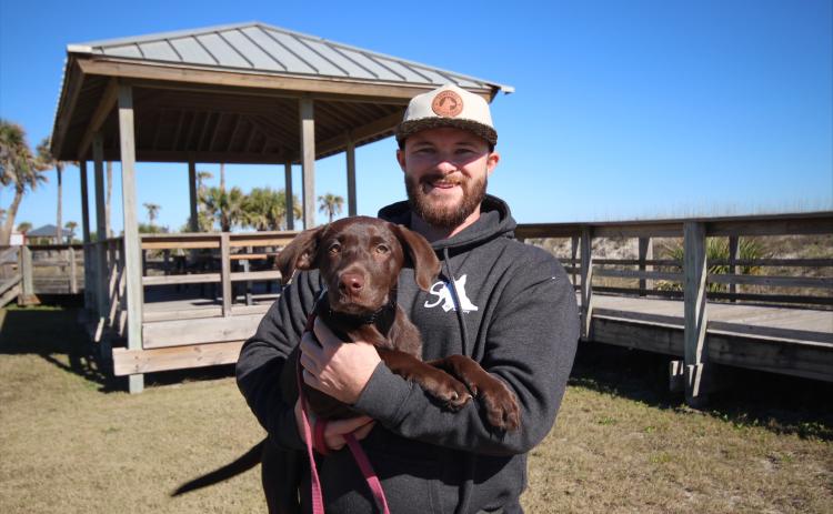 Andrew Ensign of Sentinel K9 Academy holds Daisy, the 4-month-old Labrador retriever he is training to be an autism assistance dog, at Main Beach on Dec 31. Photos by Marisa DeMar