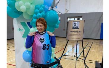 Betty Berkman stands next to a plaque with a photo of her husband, David Berkman, holding a jersey that the kids from the McArthur Family YMCA gave to her in appreciation of her generous donation to the Y. Photo by Tracy Dishman