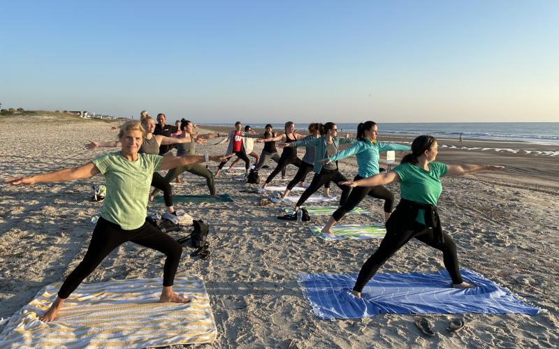 Beach yoga participants in warrior 2 pose.