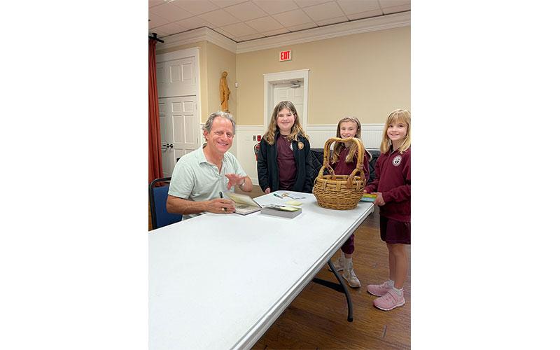 Author Stuart Gibbs signs copies of his books for the children at St. Michael Academy.